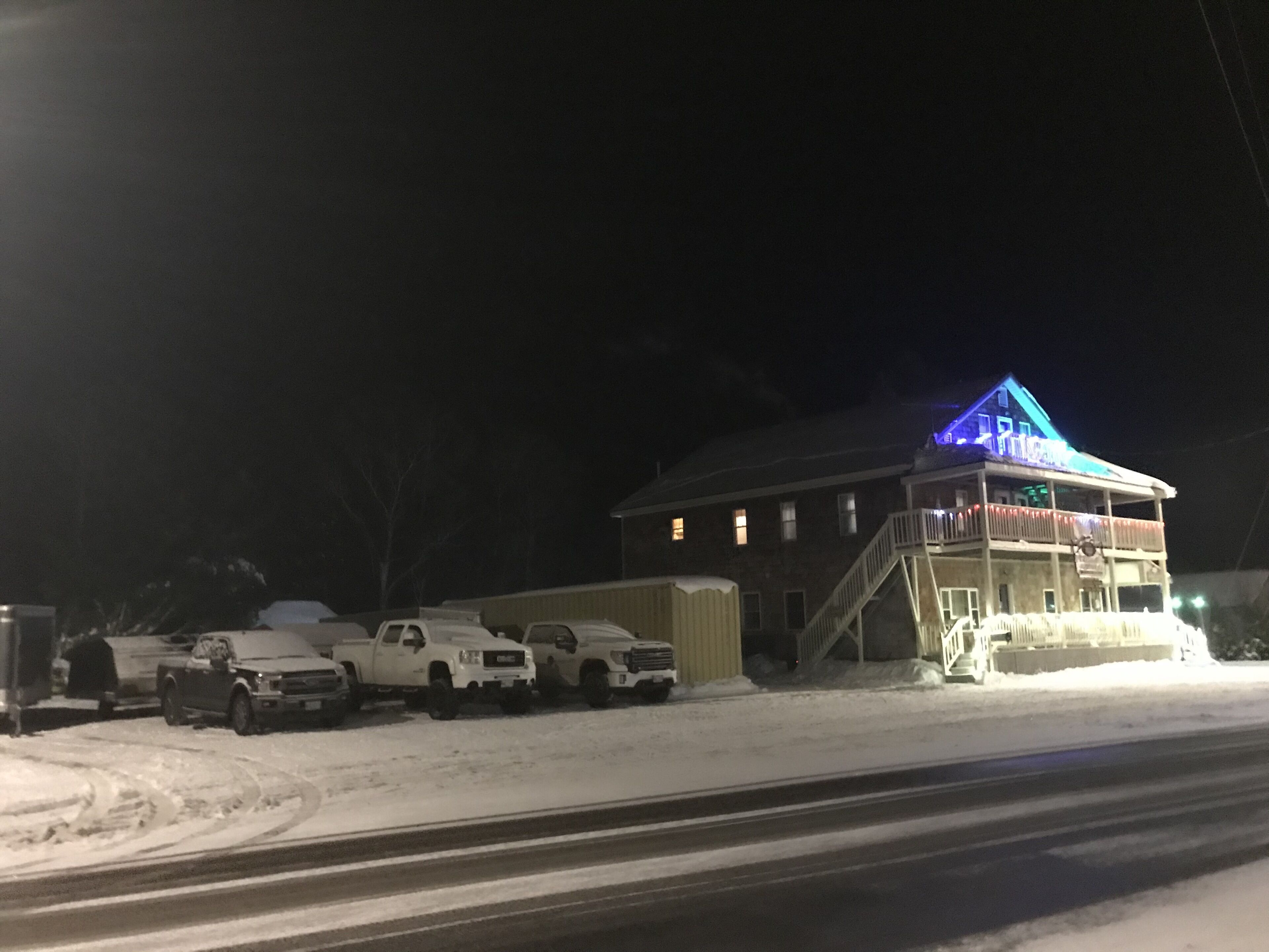 A building with a blue-lit upper level, a staircase leading to the entrance, and several parked vehicles in front.