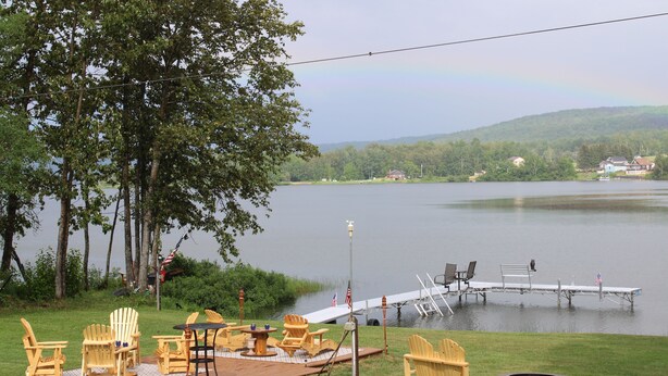 A lakeside deck with Adirondack chairs, a fire pit, and a dock extending into the water. - Majestic Recreational Lodging w/ Snowmobile and Side x Side rentals on Long Lake (Sinclair)