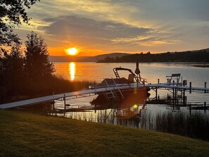 Un quai avec un bateau, une zone herbeuse et un coucher de soleil sur une étendue d’eau.