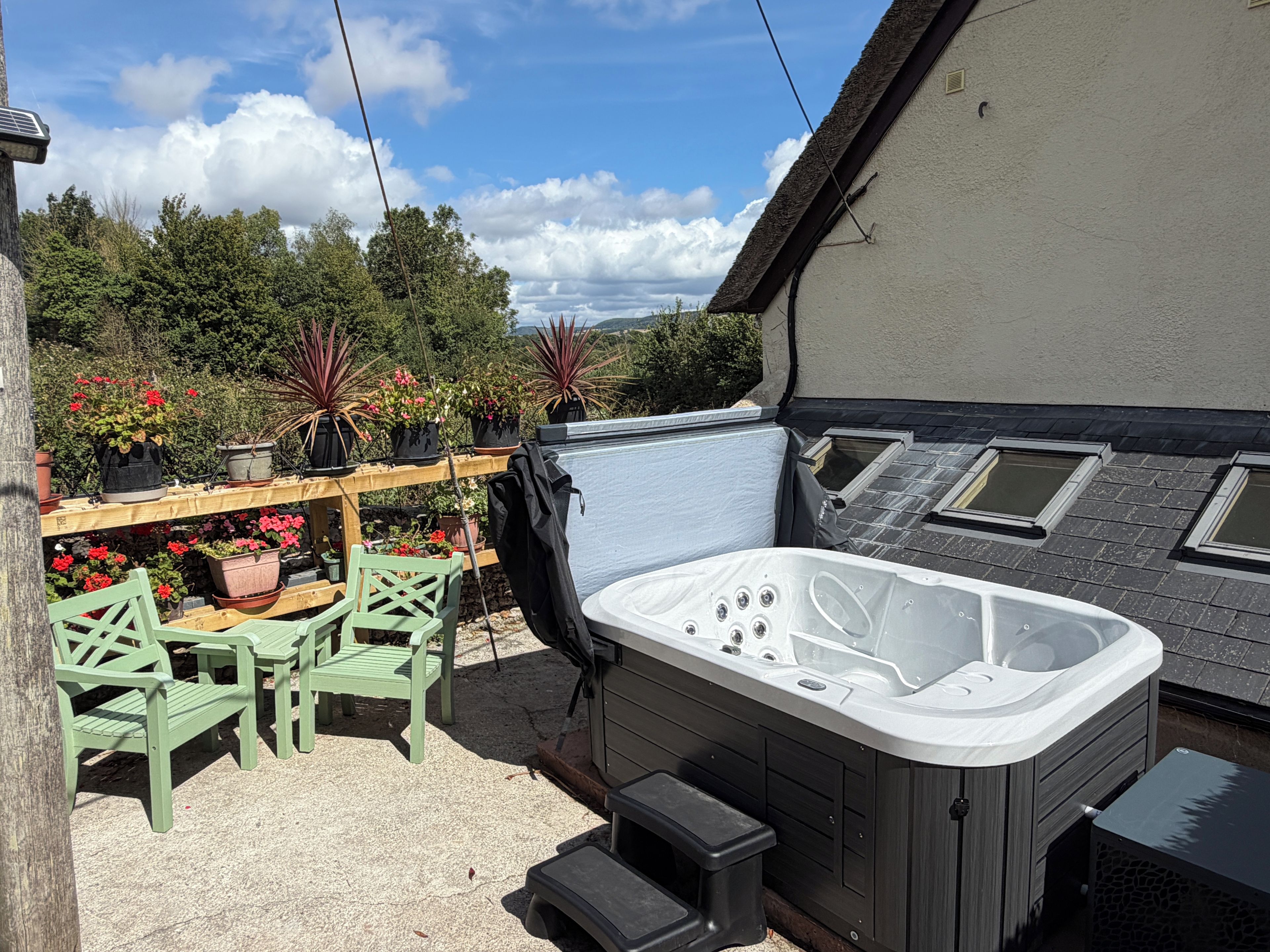 A hot tub with a wooden deck, surrounded by potted plants and outdoor furniture.