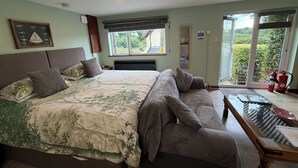 A bedroom with a large bed, a sofa, a small table, and a window with a view of greenery. - Studio in the idyllic countryside 2 miles from the beach in Devon with Hot Tub (East Budleigh)