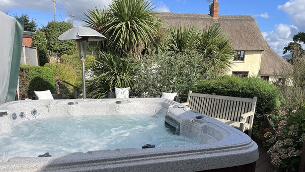 A hot tub in a garden with a thatched roof house in the background. - Studio in the idyllic countryside 2 miles from the beach in Devon with Hot Tub (East Budleigh)