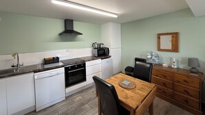 A compact kitchen with white cabinets, a black stove, a microwave, and a wooden dining table with chairs. - Studio in the idyllic countryside 2 miles from the beach in Devon with Hot Tub (East Budleigh)
