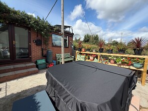 A covered outdoor seating area with a table and benches, surrounded by potted plants and a brick building with a window. - Studio in the idyllic countryside 2 miles from the beach in Devon with Hot Tub (East Budleigh)