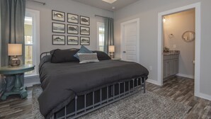 Une chambre à coucher avec un grand lit, deux tables de chevet avec des lampes, une fenêtre avec des rideaux et une porte donnant sur une salle de bain.