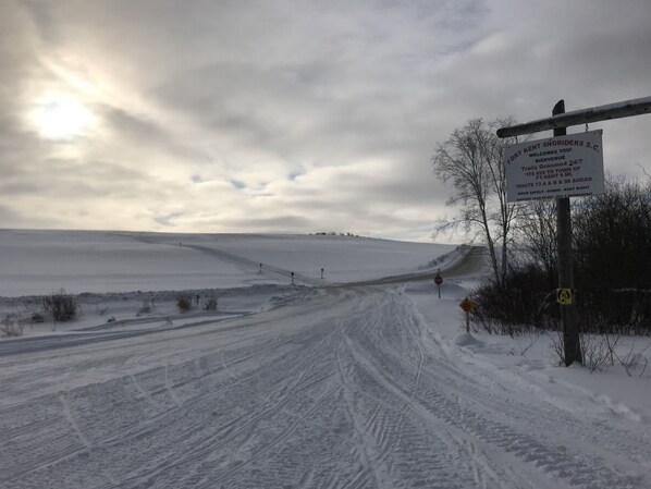 A snowy landscape with a sign for Fort Kent Snowdrifts S.C. and a dirt road. - Majestic Recreational Lodging w/ Snowmobile and Side x Side rentals on Long Lake (Sinclair)