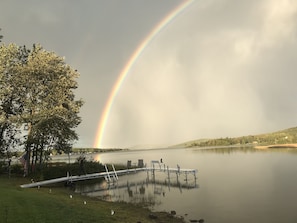 A lake with a dock, trees, and a rainbow.