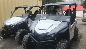 Two off-road vehicles parked in a lot with a building in the background. - Majestic Recreational Lodging w/ Snowmobile and Side x Side rentals on Long Lake (Sinclair)