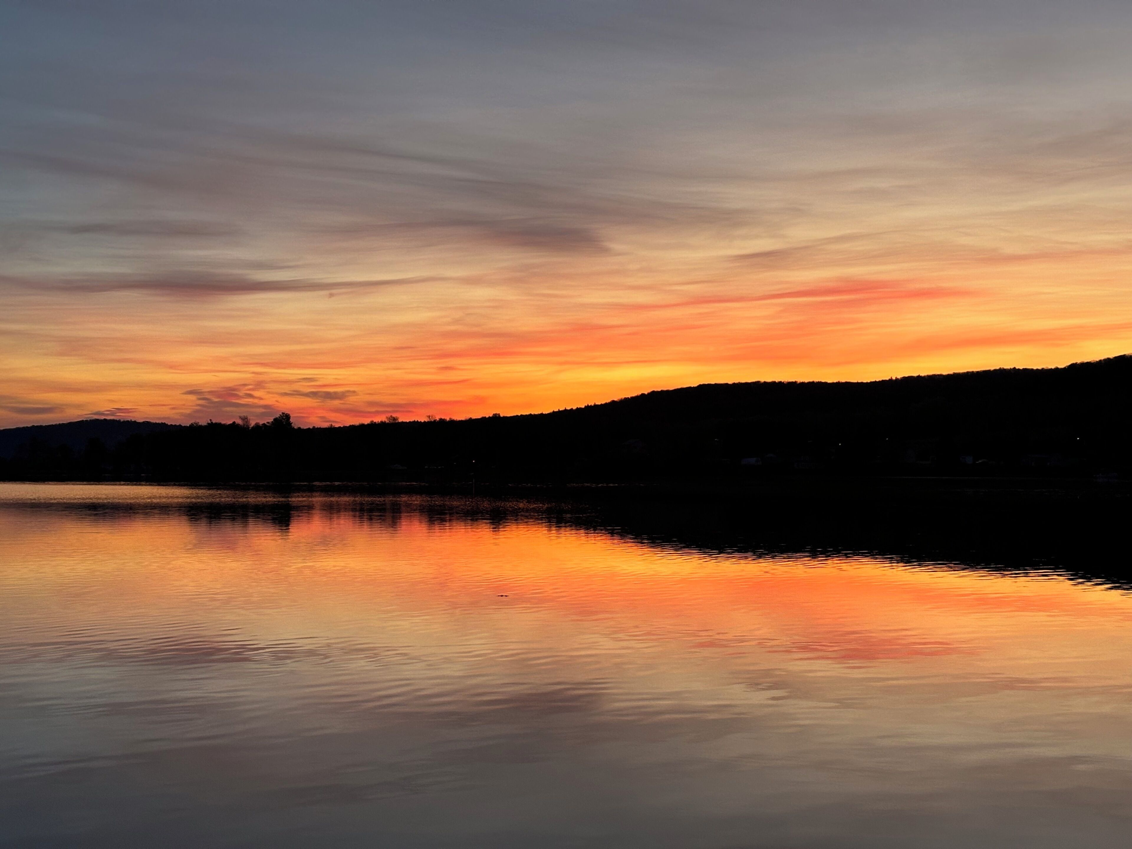 Ein stiller See, der einen Sonnenuntergang widerspiegelt, mit einer Hügelsilhouette im Hintergrund.