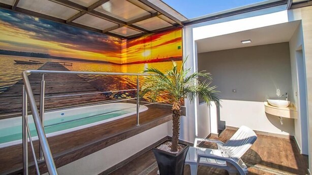 A modern indoor pool area with a sunset mural, a small palm tree, and a lounge chair. - Hotel Zaragoza Inn Boutique (Mexico City)
