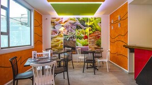 A restaurant interior with tables and chairs, a counter, and a mural of food on the wall. - Hotel Zaragoza Inn Boutique (Mexico City)
