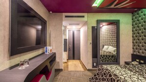 A hotel room with a large bed, a TV mounted on the wall, a desk with a computer, and a mirror. - Hotel Zaragoza Inn Boutique (Mexico City)