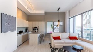 A modern apartment with a kitchen, a living area with a sofa and a coffee table, and large windows offering a city view. - Panoramic bay views meet modern elegance in this 1-bedroom retreat (Hollywood)