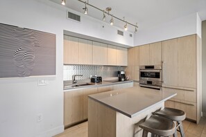 A modern kitchen with a central island, built-in appliances, and a striped wall decoration. - Panoramic bay views meet modern elegance in this 1-bedroom retreat (Hollywood)