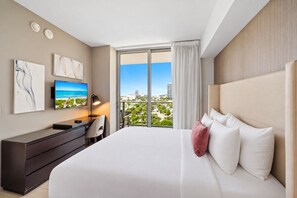 Ein Hotelzimmer mit einem großen Bett, einem Schreibtisch, einem Fernseher und einem Balkon mit Blick auf die Stadt.