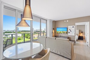 A modern hotel room with a balcony, a round dining table, a sofa, a TV, and a painting on the wall. - Panoramic bay views meet modern elegance in this 1-bedroom retreat (Hollywood)