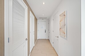 A hallway with white doors, a wooden floor, and a ceiling light. - Panoramic bay views meet modern elegance in this 1-bedroom retreat (Hollywood)