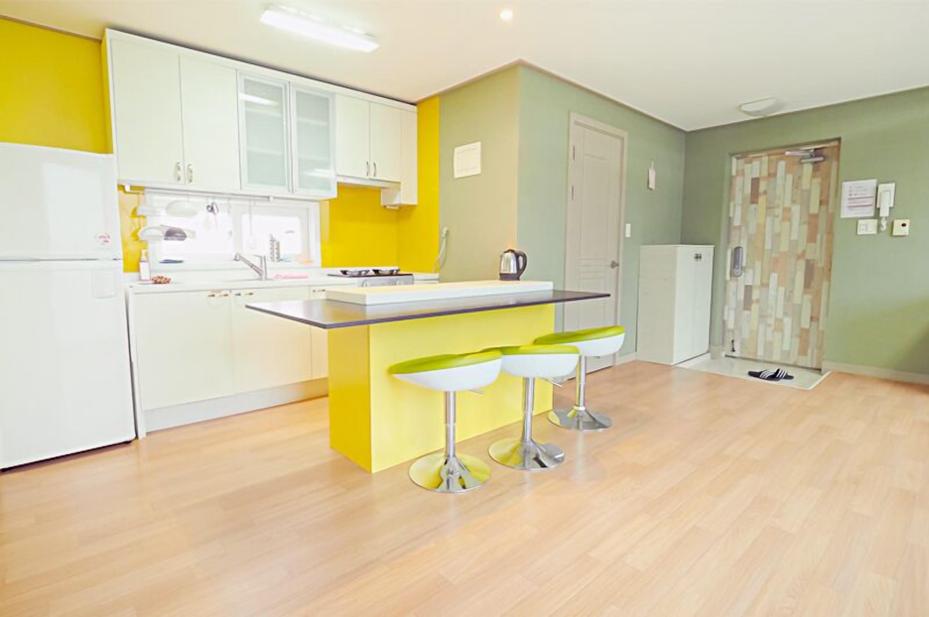 Une cuisine moderne avec des meubles blancs, un îlot de couleur jaune et trois tabourets de bar.