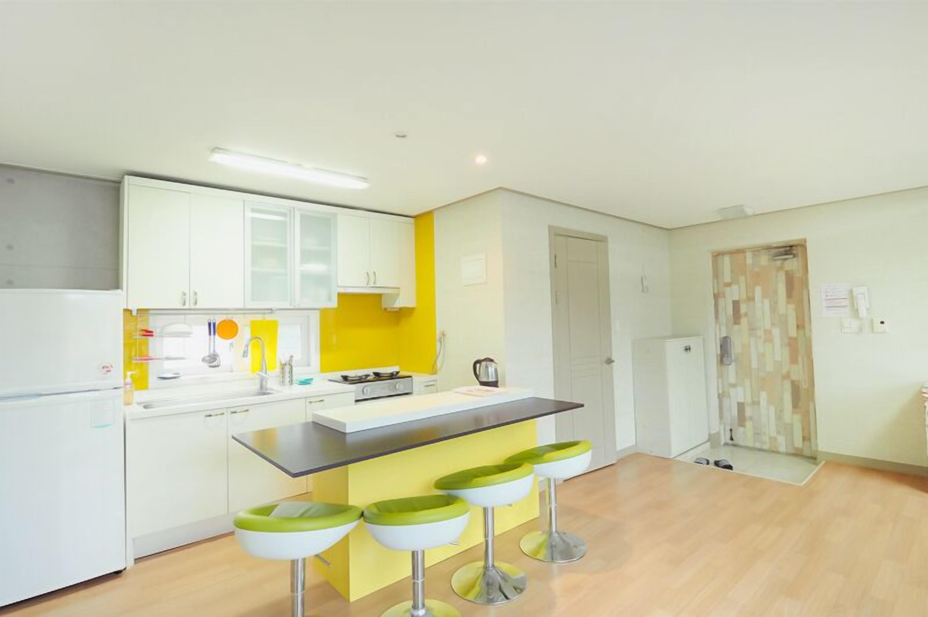 Una cocina moderna con armarios blancos, una pared de acento amarilla, encimera negra y tres taburetes verdes.