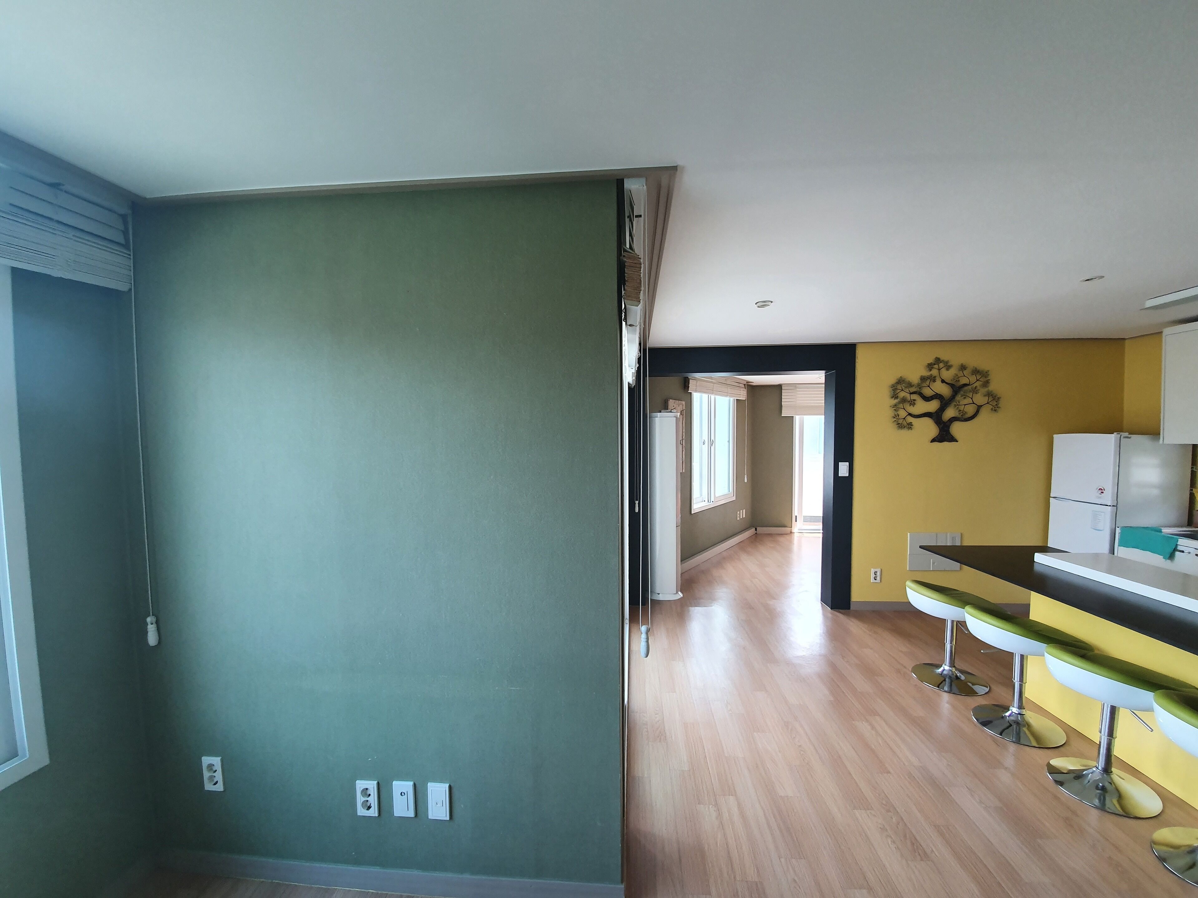 Cocina moderna con una pared de acento amarilla, suelo de madera y una barra con taburetes.