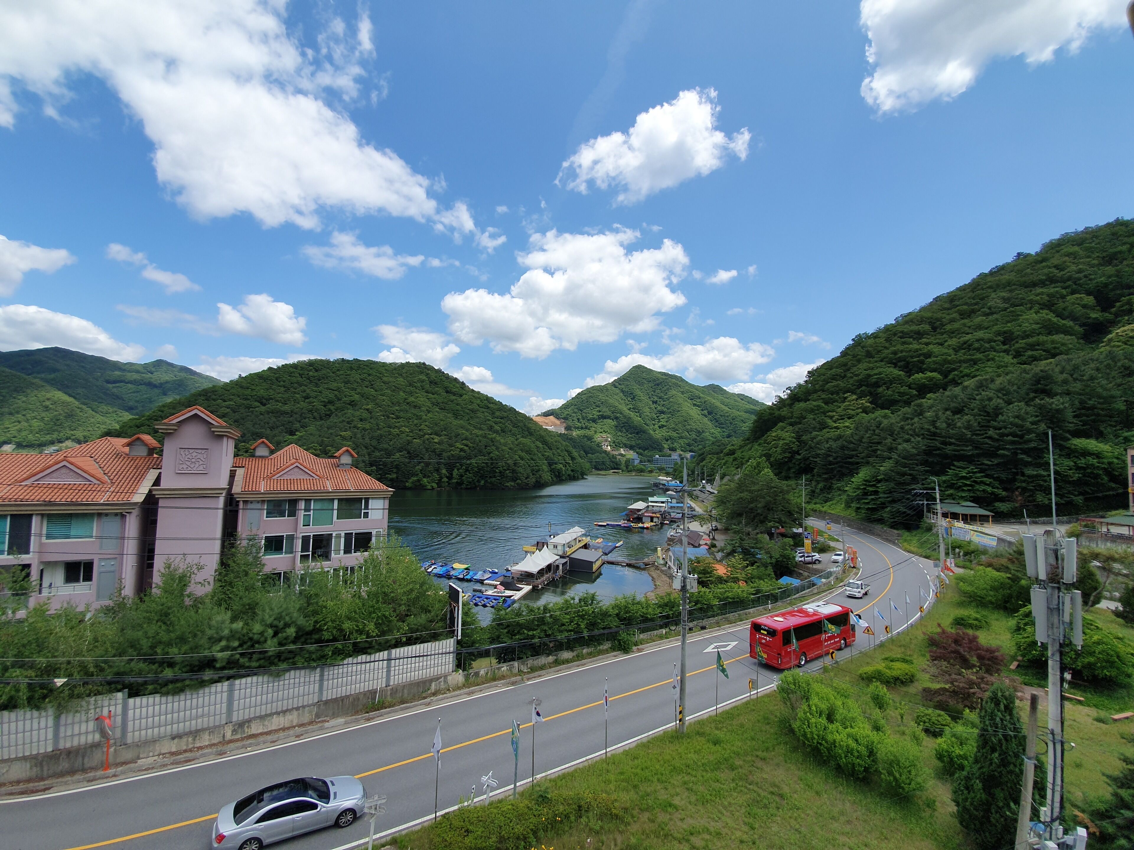 A coastal road with a red bus, a car, and a row of houses with red roofs.