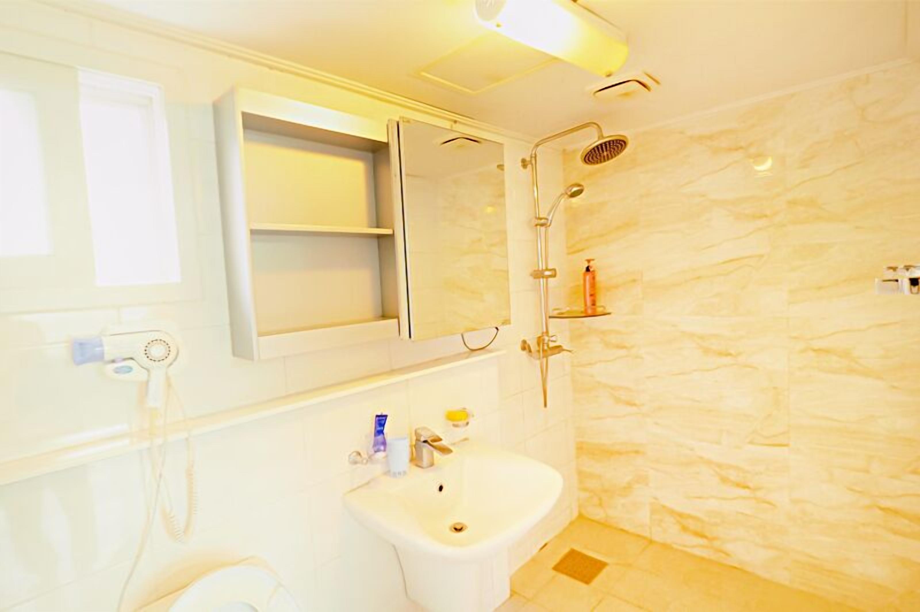 A bathroom with a white sink, a mirror, a shower, and a marble wall.