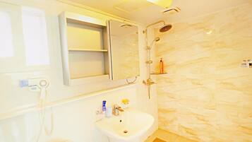 A bathroom with a white sink, a mirror, a shower, and a marble wall.