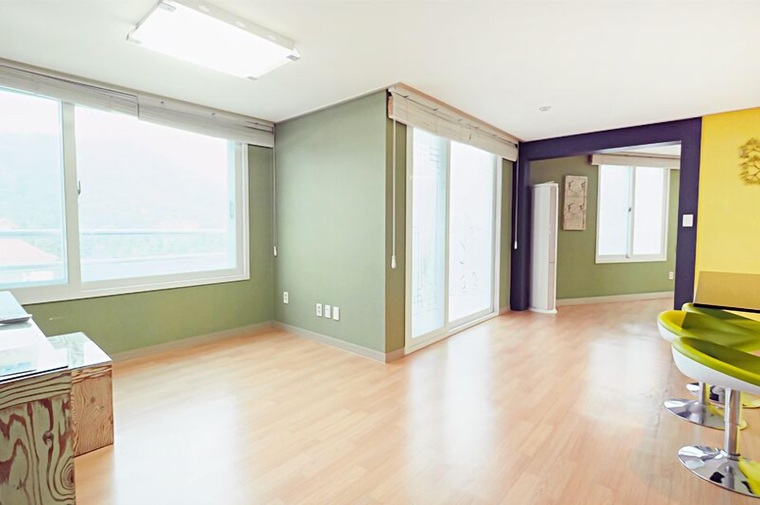 A spacious room with large windows, a wooden floor, and a green wall.