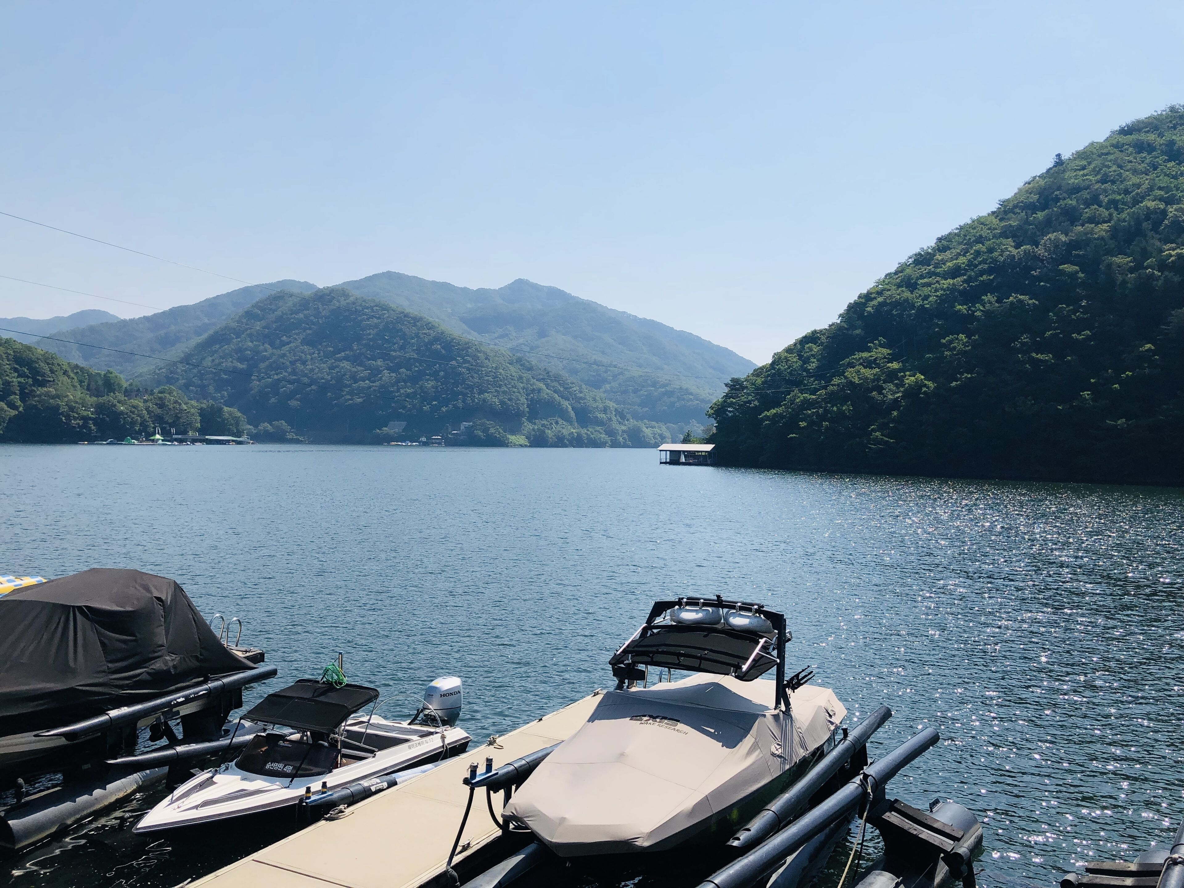Un port de plaisance avec des bateaux amarrés, une zone abritée et, en arrière-plan, des montagnes et un lac.
