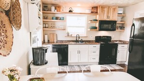 A kitchen with white cabinets, a black refrigerator, and a microwave. There is a window above the sink and a vase with flowers on the counter. - Home with gated driveway near River & Downtown (Grants Pass)