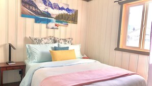A bedroom with a bed, pillows, a bedside table, a lamp, and a window.