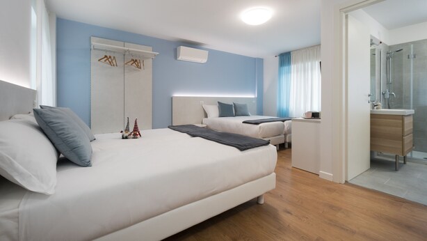 A modern hotel room with a large bed, a smaller bed, a desk, and a shower area. - Zona 30 Bike Guesthouse (Palmanova)