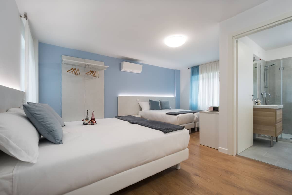 A modern hotel room with a large bed, a smaller bed, a desk, and a shower area.