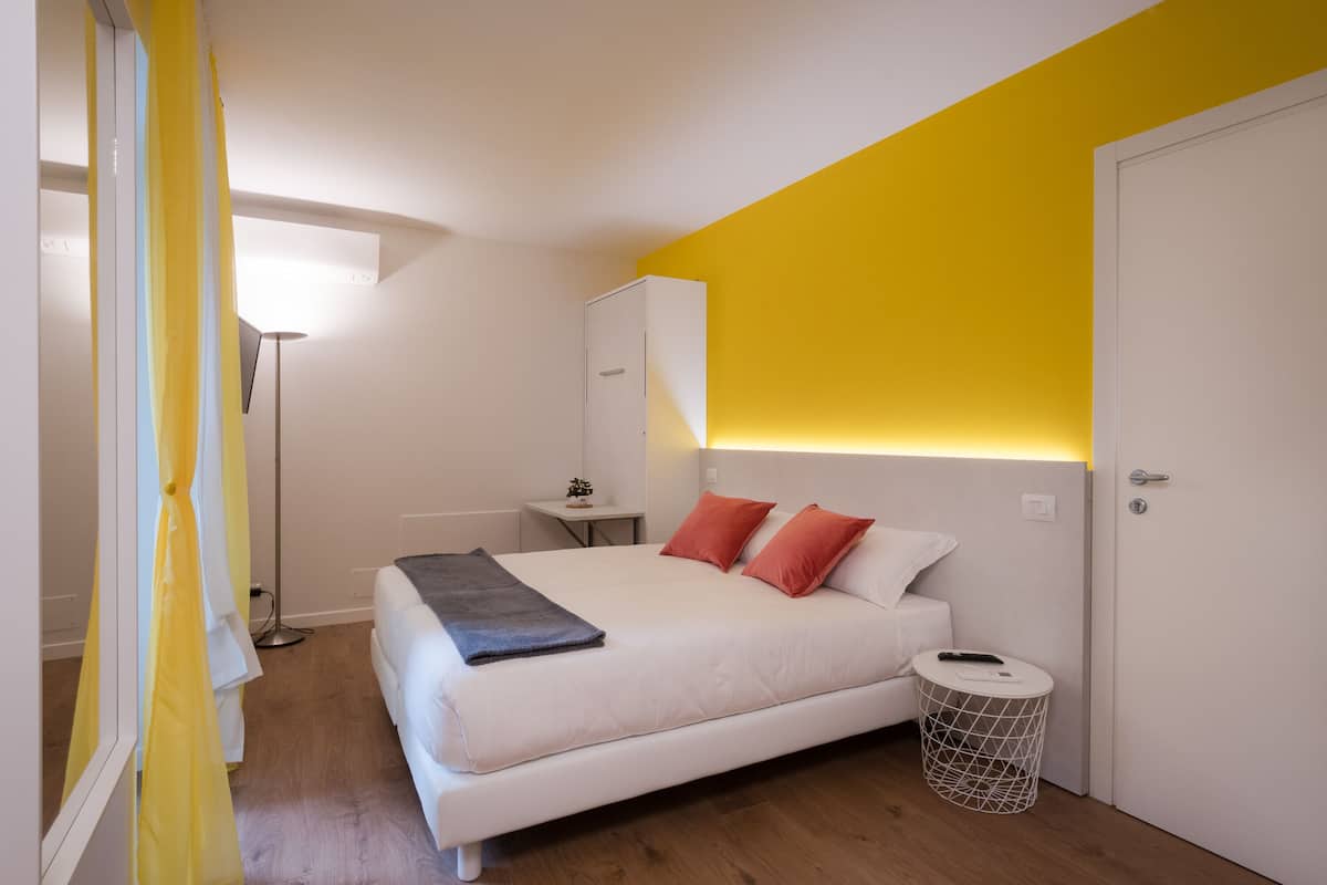 A modern bedroom with a white bed, yellow accent wall, and a bedside table with a lamp.