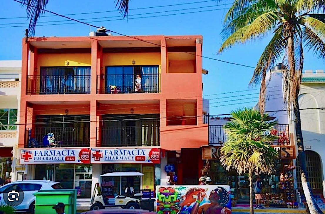 A multi-story building with two pharmacy signs, a green trash bin, and a parked vehicle.