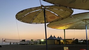 A beachside restaurant with outdoor seating, umbrellas, and a view of the beach.