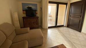 A living room with a sofa, a television on a wooden cabinet, and a sliding glass door leading to an outdoor area.
