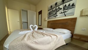 A neatly made bed with a quilt, a painting on the wall, and a wooden headboard.