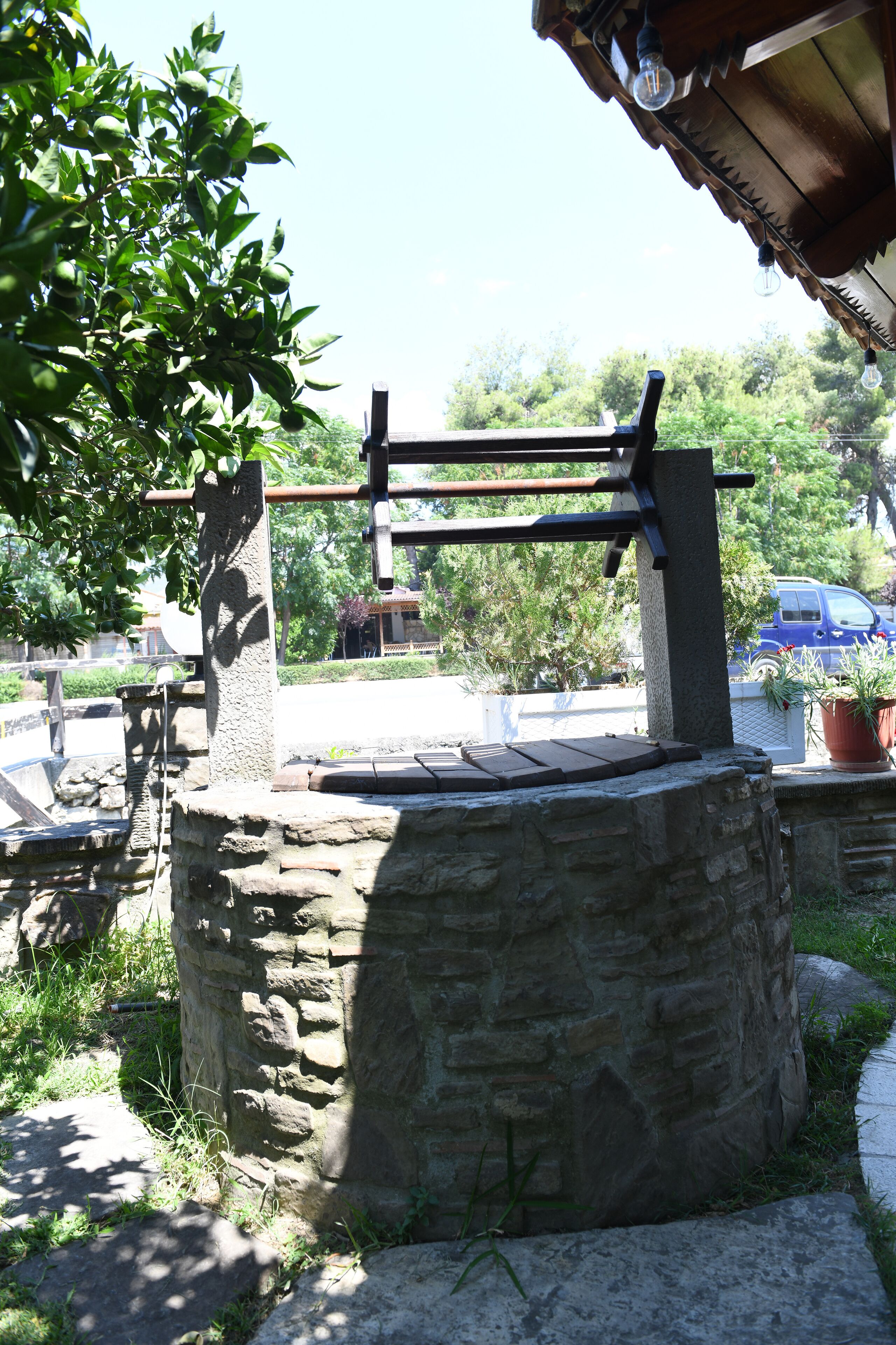 A stone structure with a wooden bench, surrounded by greenery and a car in the background.