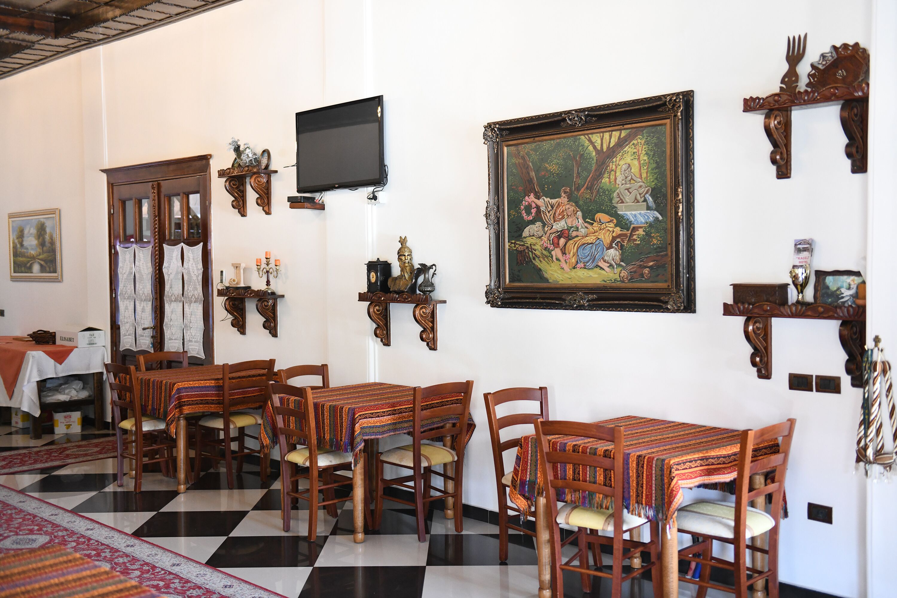 A dining area with wooden tables and chairs, a black and white checkered floor, and a painting on the wall.