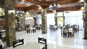 A spacious restaurant with stone pillars, wooden beams, and chandeliers. Tables are set with white tablecloths and chairs. - Hotel Kaceli (Berat)