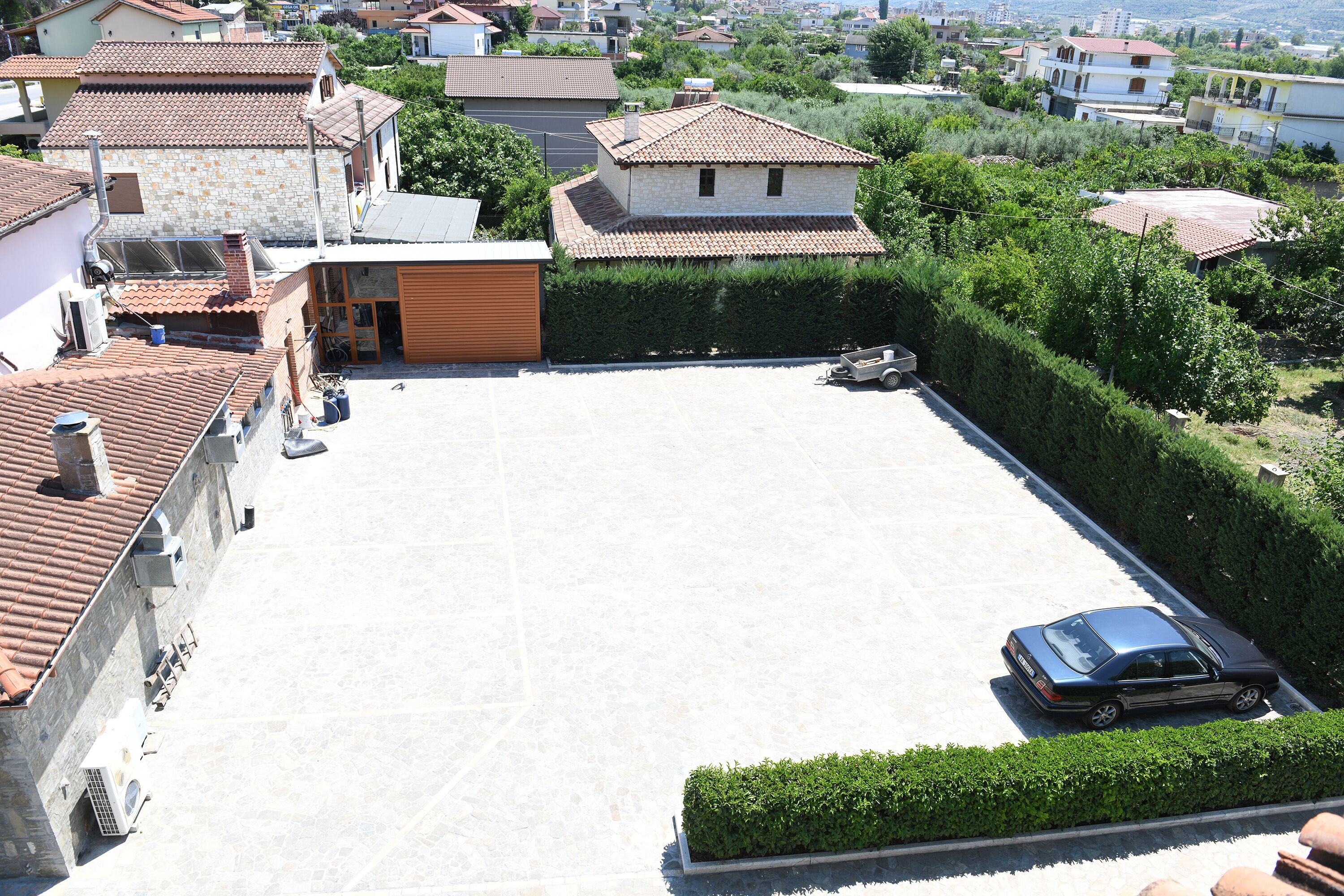 A residential area with a large open space, a parked car, and surrounding houses with tiled roofs.