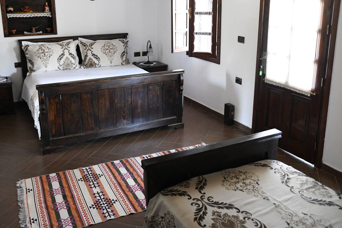A bedroom with a wooden bed, a chandelier, a wooden ceiling, and a window with curtains.