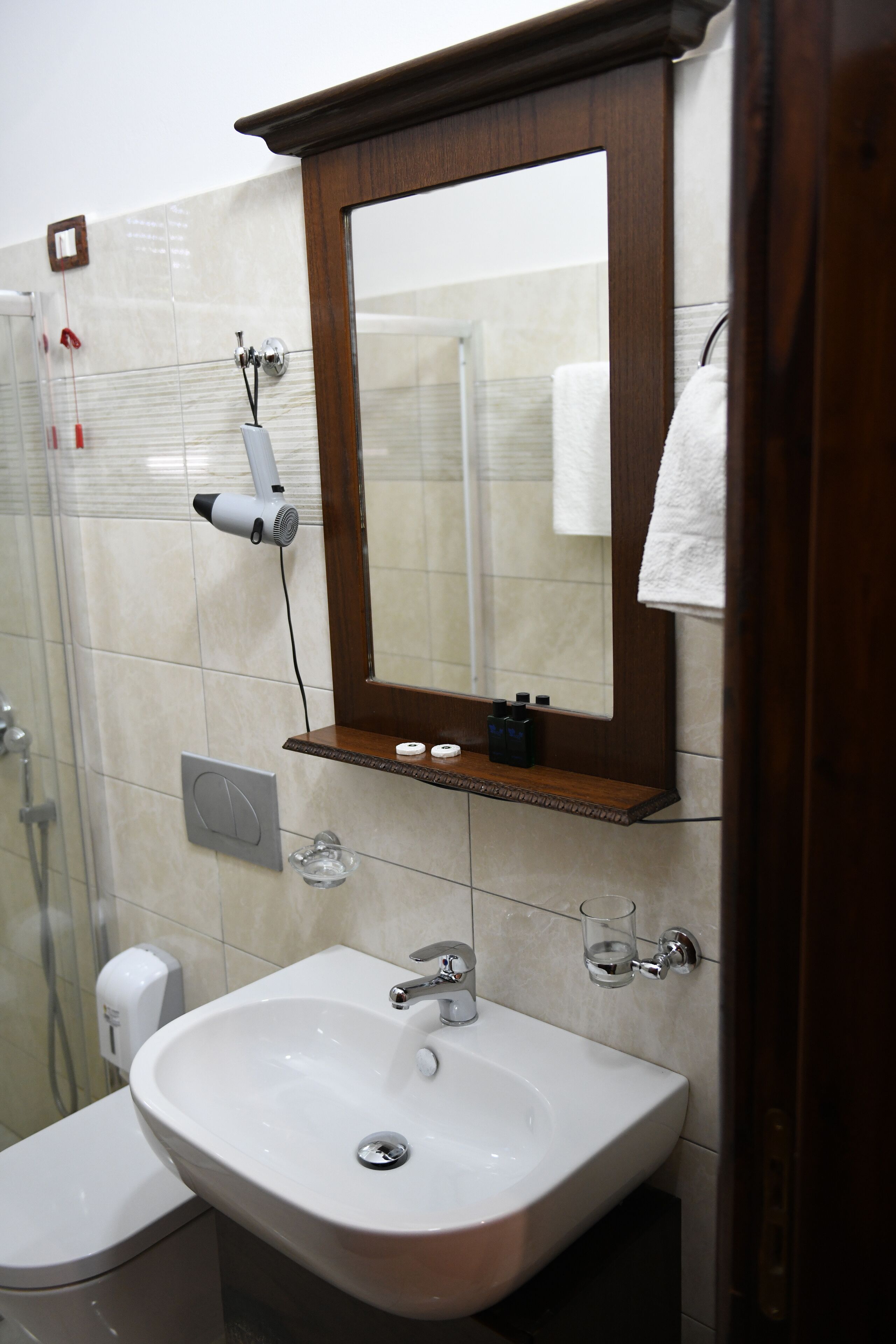 A bathroom with a white sink, a mirror, and a hairdryer mounted on the wall.