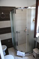Box de chuveiro com paredes de vidro, vaso sanitário branco e lixeira à direita.