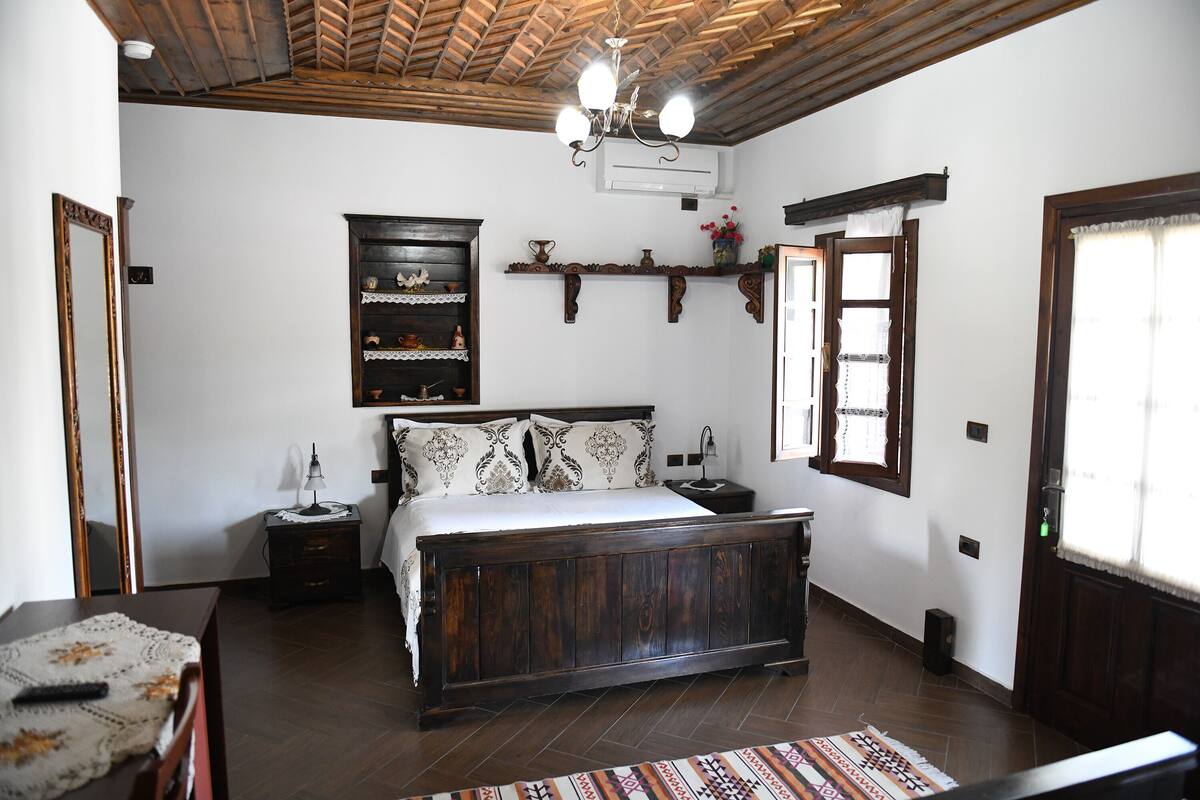 A bedroom with a wooden bed, a nightstand, a dresser, a mirror, and a chandelier.