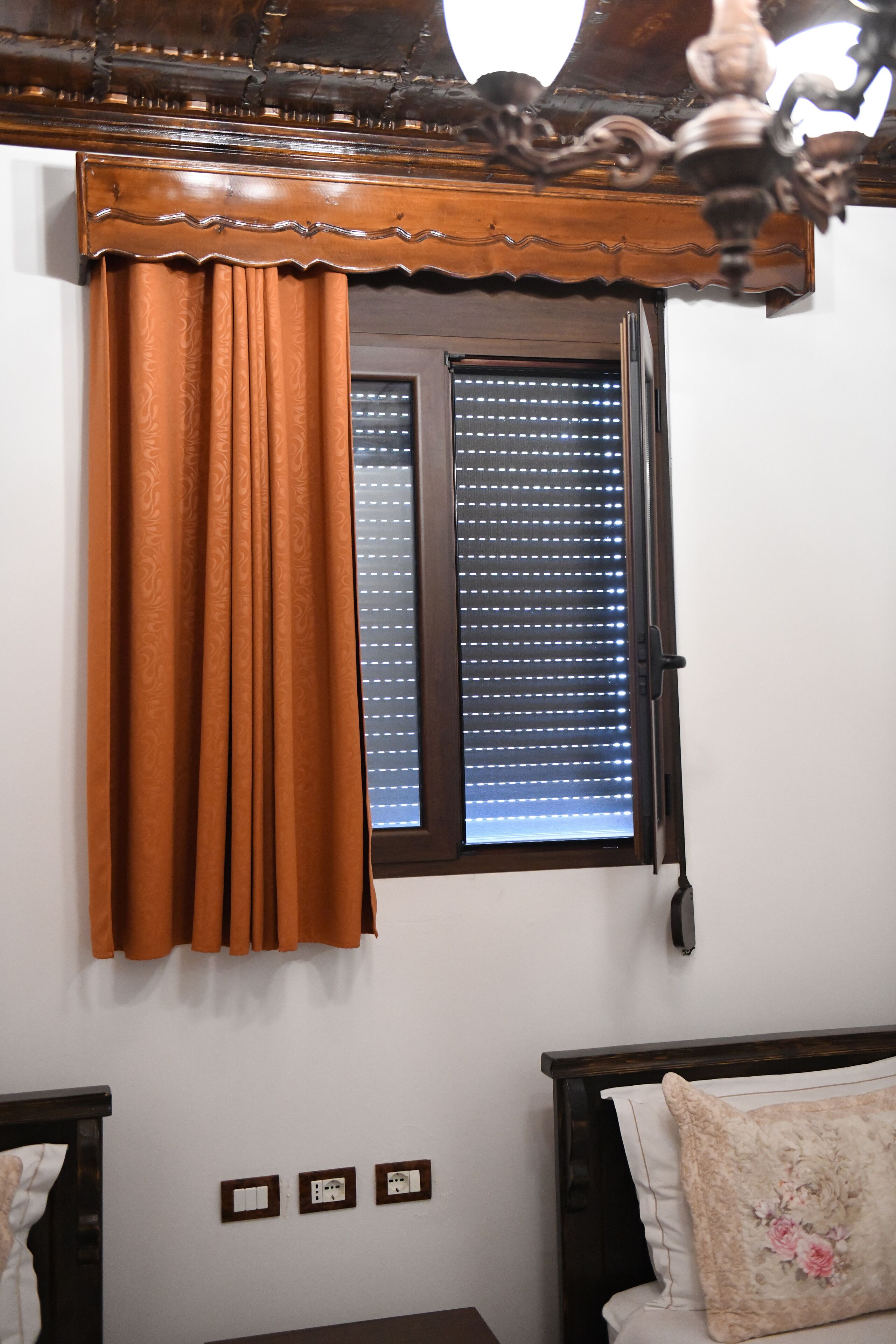 Un dormitorio con ventana, cortinas, una cama y una mesita de noche.