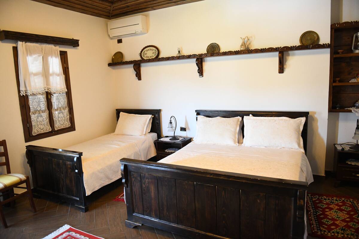 A room with two wooden beds, a chair, a shelf with decorative plates, and a red rug.