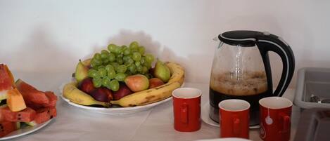 A table with a fruit platter, a coffee pot, and red cups.