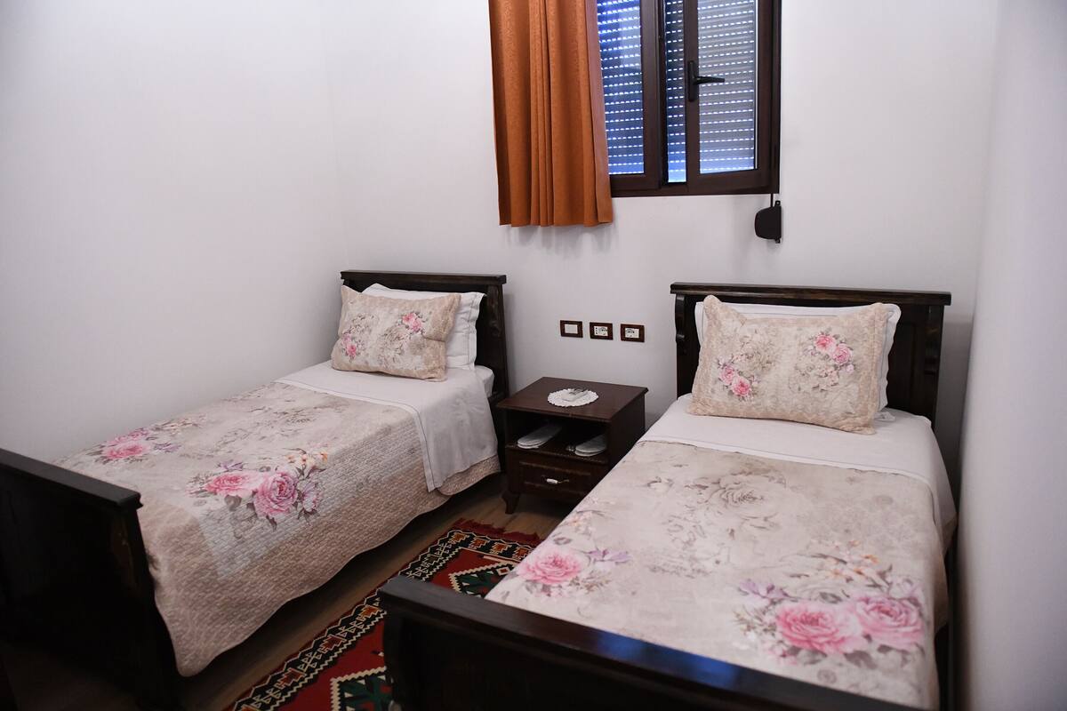 A bedroom with two single beds, each with floral bedding and a small nightstand.